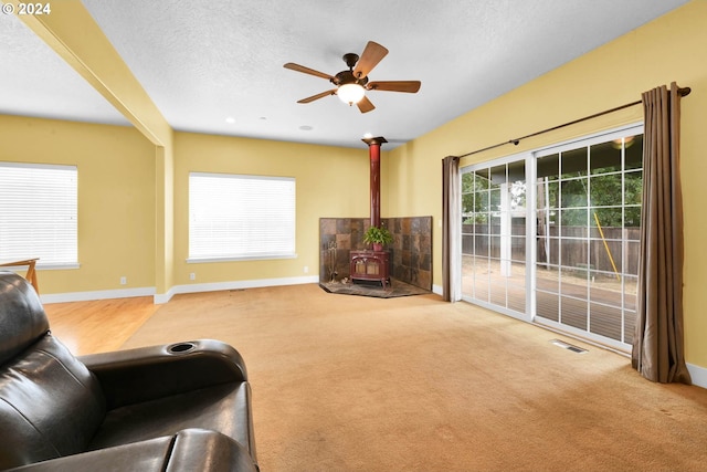 living room with a wood stove, a wealth of natural light, a textured ceiling, and carpet flooring