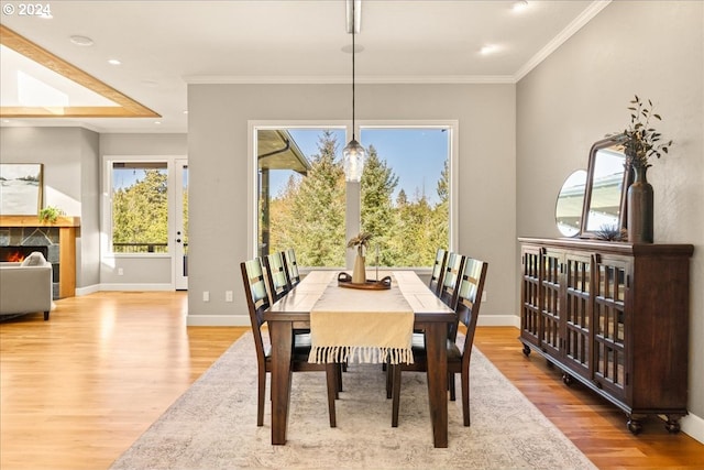 dining area featuring light wood-type flooring, ornamental molding, and a tiled fireplace