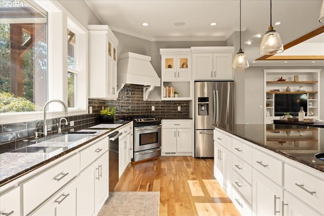 kitchen featuring sink, white cabinetry, dark stone counters, stainless steel appliances, and hanging light fixtures