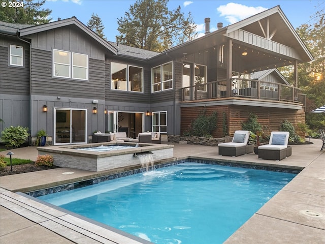 rear view of house featuring a swimming pool with hot tub, pool water feature, a balcony, and a patio area