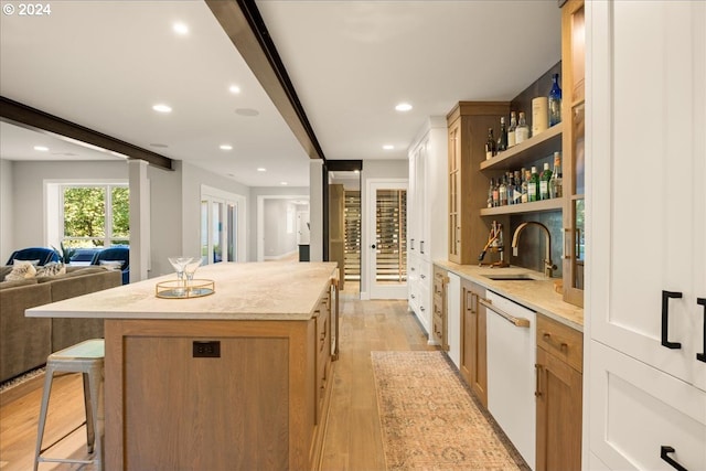 kitchen featuring sink, dishwasher, beamed ceiling, light hardwood / wood-style floors, and a breakfast bar area