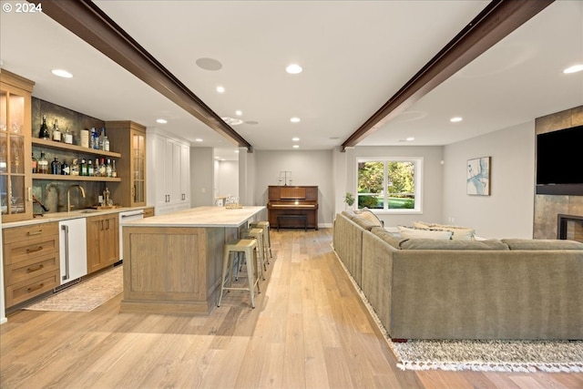 bar with light hardwood / wood-style flooring, dishwasher, a tiled fireplace, beamed ceiling, and sink