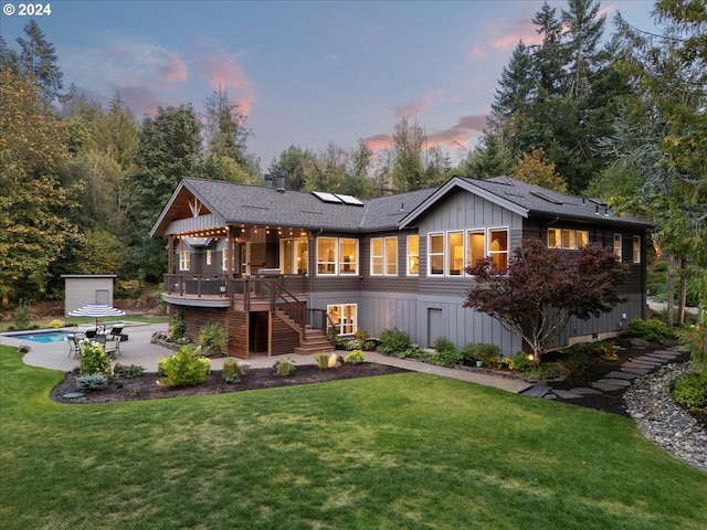 back house at dusk featuring solar panels, a patio area, a swimming pool side deck, and a lawn