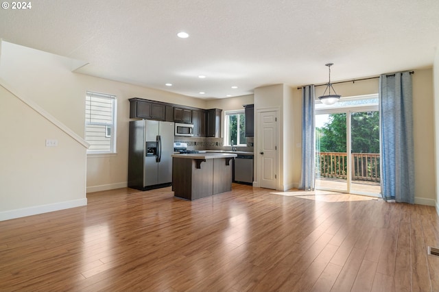 kitchen with a wealth of natural light, appliances with stainless steel finishes, dark brown cabinetry, and light hardwood / wood-style flooring