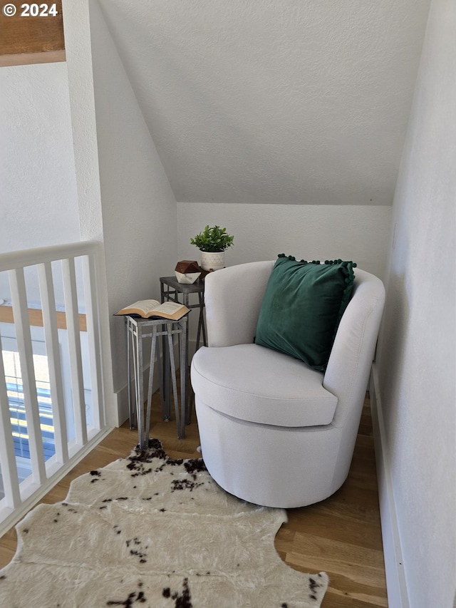 sitting room featuring wood-type flooring, vaulted ceiling, and a textured ceiling