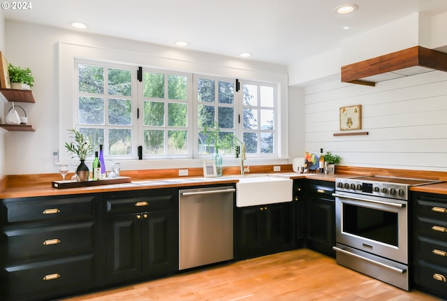 kitchen with stainless steel appliances, premium range hood, wooden counters, and light hardwood / wood-style floors