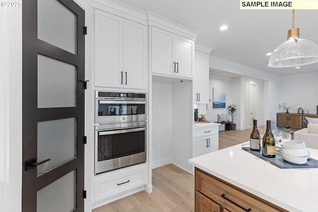 kitchen featuring white cabinetry, stainless steel double oven, decorative light fixtures, and light hardwood / wood-style floors