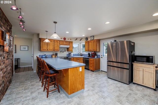 kitchen with appliances with stainless steel finishes, a kitchen breakfast bar, pendant lighting, and brick wall