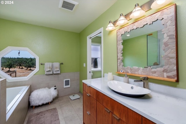 bathroom with tile walls, tile patterned flooring, tiled tub, and vanity