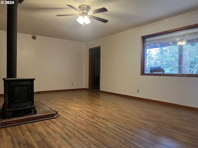 unfurnished living room featuring hardwood / wood-style flooring, a wood stove, a textured ceiling, and ceiling fan