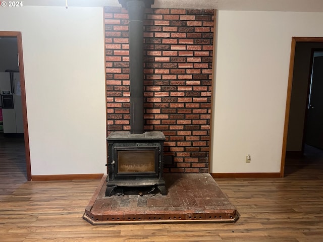 room details with white refrigerator with ice dispenser, a wood stove, and hardwood / wood-style floors