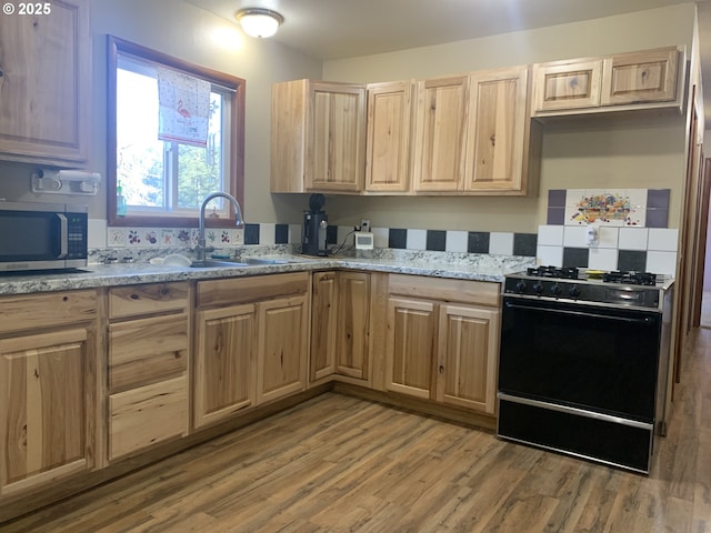 kitchen featuring black range with gas cooktop, light brown cabinetry, sink, light wood-type flooring, and light stone countertops