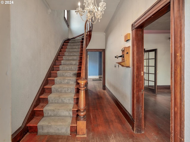 stairs with ornamental molding, hardwood / wood-style floors, and an inviting chandelier