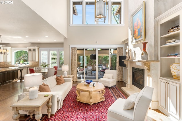 living room featuring a notable chandelier, light wood-type flooring, a fireplace, and a towering ceiling