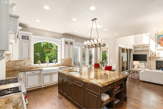 kitchen featuring tasteful backsplash, dark brown cabinets, an island with sink, and sink