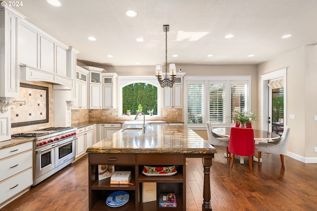 kitchen with double oven range, a kitchen island with sink, dark wood-type flooring, hanging light fixtures, and light stone counters