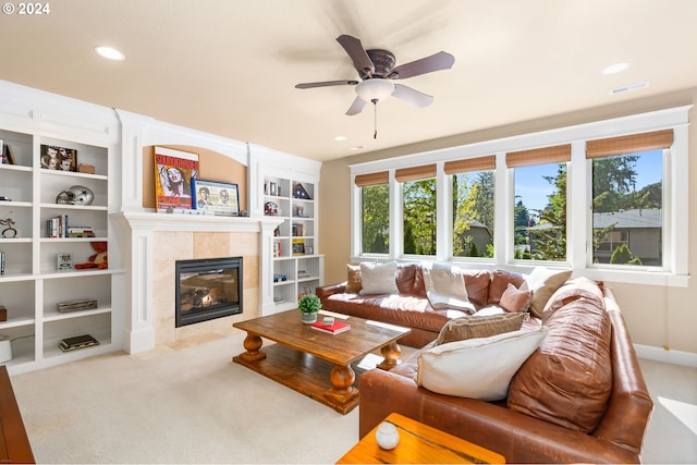 carpeted living room featuring ceiling fan, built in features, and a tiled fireplace