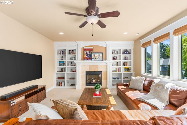 living room with ceiling fan, built in features, light carpet, and a tiled fireplace