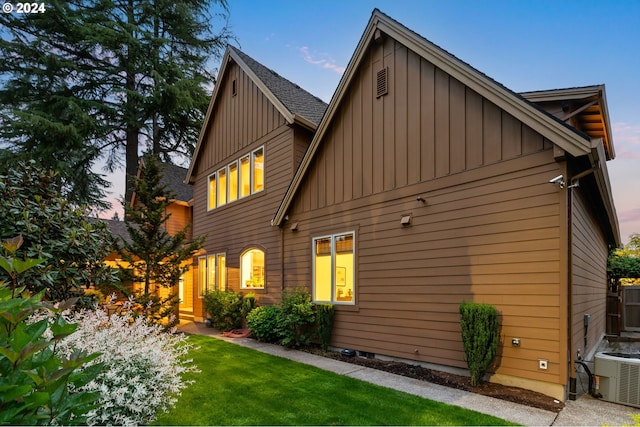 property exterior at dusk with central AC and a lawn