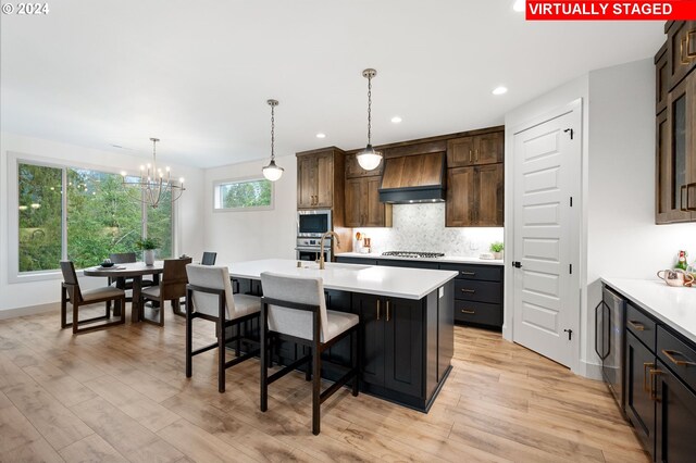 kitchen with light hardwood / wood-style floors, an island with sink, appliances with stainless steel finishes, custom range hood, and dark brown cabinetry