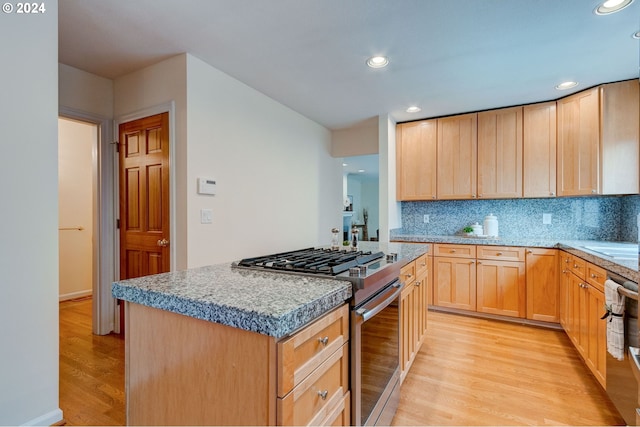 kitchen with a kitchen island, decorative backsplash, light brown cabinets, light wood-type flooring, and appliances with stainless steel finishes