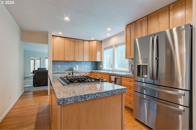 kitchen featuring decorative backsplash, light hardwood / wood-style flooring, stainless steel appliances, sink, and a center island