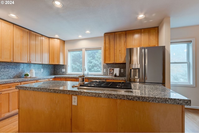 kitchen with backsplash, appliances with stainless steel finishes, light hardwood / wood-style floors, and an island with sink