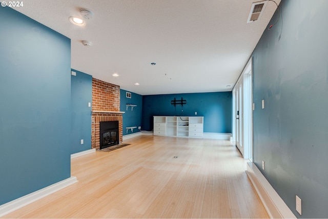 unfurnished living room with a textured ceiling, a brick fireplace, and hardwood / wood-style floors