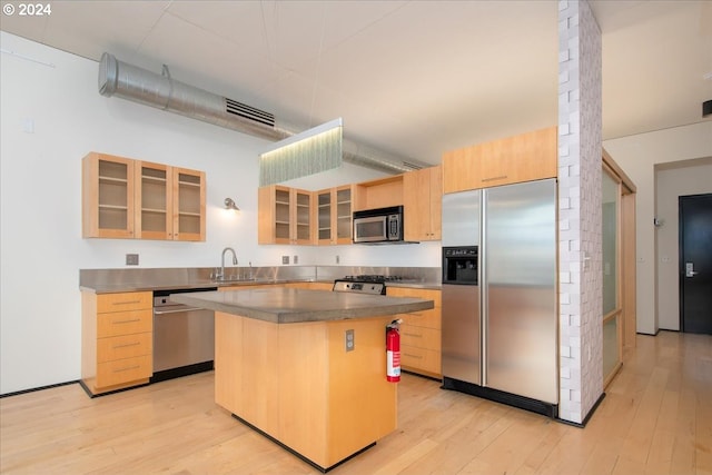 kitchen with brick wall, appliances with stainless steel finishes, a center island, and light wood-type flooring