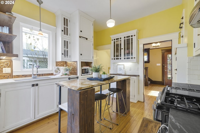 kitchen with a breakfast bar area, decorative backsplash, white cabinetry, and hanging light fixtures