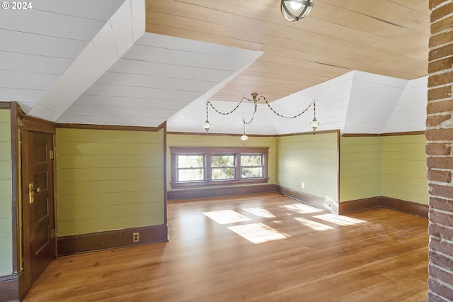 additional living space with wood walls, vaulted ceiling, and hardwood / wood-style flooring