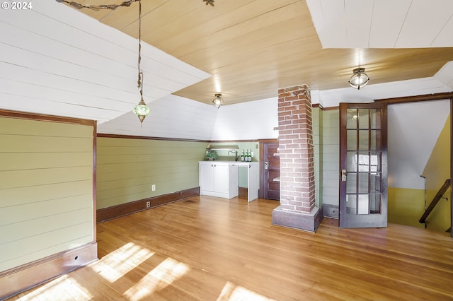 unfurnished living room featuring decorative columns, wood ceiling, vaulted ceiling, wooden walls, and hardwood / wood-style floors