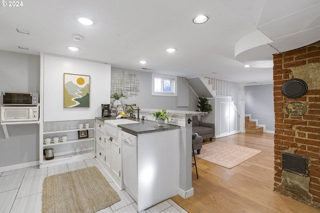 kitchen featuring white appliances, white cabinets, sink, light wood-type flooring, and a breakfast bar area