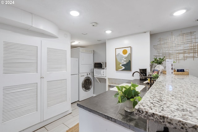 laundry area featuring stacked washing maching and dryer, sink, and light hardwood / wood-style flooring