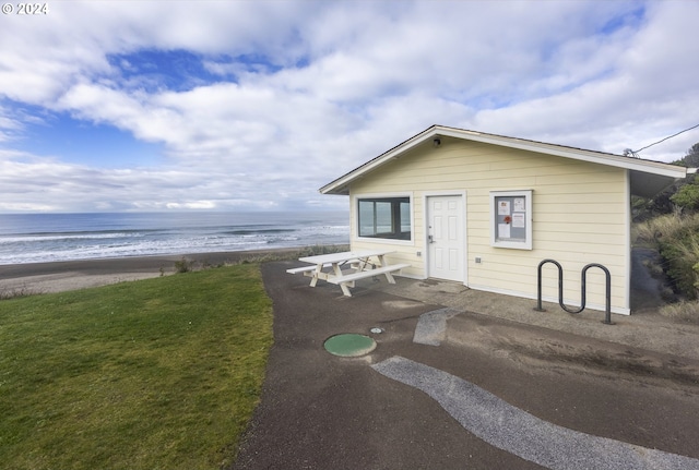 view of front of property featuring a front yard, a patio, a beach view, and a water view