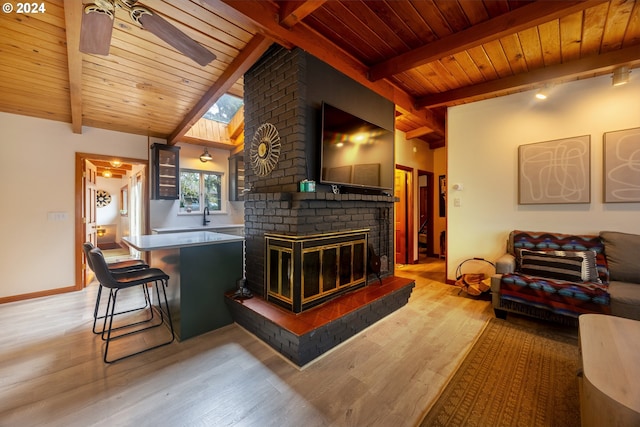 bar featuring ceiling fan, lofted ceiling with skylight, a brick fireplace, and light hardwood / wood-style flooring