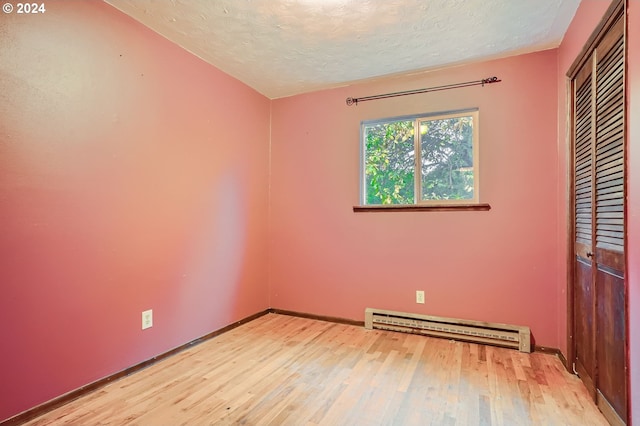 unfurnished bedroom featuring a closet, baseboard heating, light wood-type flooring, and a textured ceiling