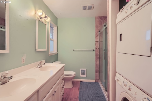 bathroom with toilet, a shower with door, stacked washing maching and dryer, and hardwood / wood-style flooring