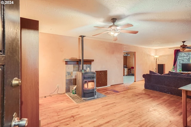 living room featuring a wood stove, ceiling fan, light hardwood / wood-style floors, and a textured ceiling