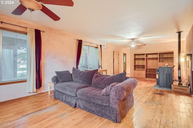 living room featuring a textured ceiling, light wood-type flooring, a wood stove, and ceiling fan