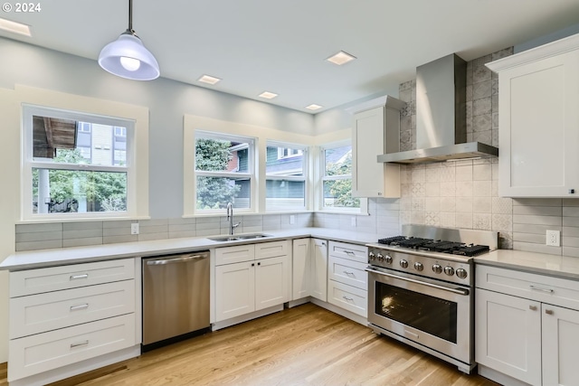 kitchen with appliances with stainless steel finishes, sink, decorative light fixtures, wall chimney range hood, and white cabinets