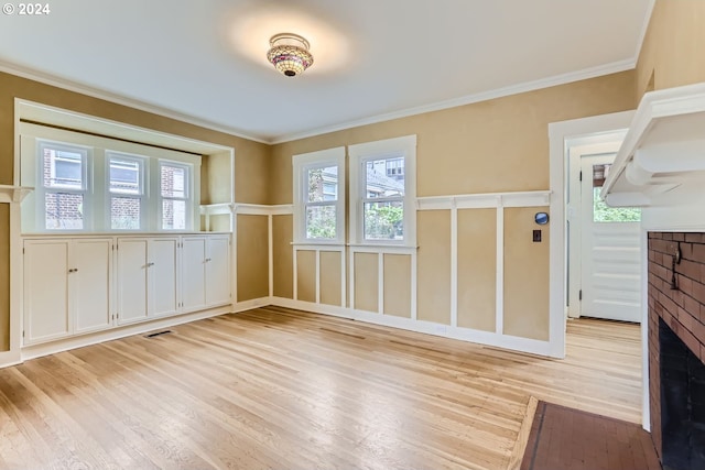 unfurnished dining area with a brick fireplace, light hardwood / wood-style flooring, and ornamental molding