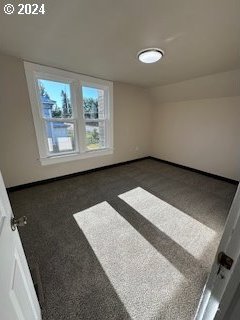 empty room featuring lofted ceiling and dark colored carpet