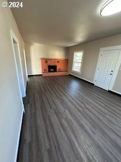 unfurnished living room featuring dark hardwood / wood-style flooring and a brick fireplace