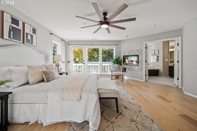 bedroom with ceiling fan, access to outside, light hardwood / wood-style floors, a high end fireplace, and ensuite bathroom