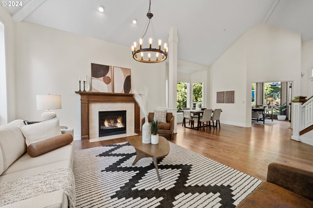 living room with a fireplace, an inviting chandelier, high vaulted ceiling, and hardwood / wood-style flooring