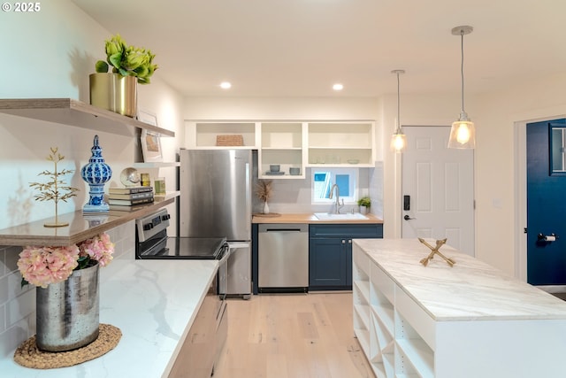 kitchen featuring appliances with stainless steel finishes, stacked washer / dryer, blue cabinets, decorative light fixtures, and light hardwood / wood-style flooring