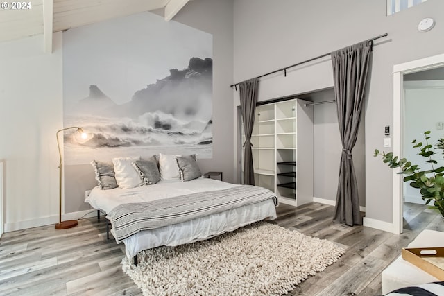 bedroom featuring beam ceiling, light hardwood / wood-style flooring, high vaulted ceiling, and a closet