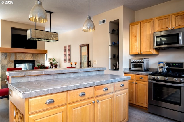 kitchen featuring decorative light fixtures, built in features, appliances with stainless steel finishes, a multi sided fireplace, and dark hardwood / wood-style flooring