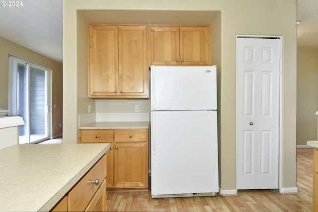 kitchen with light brown cabinets, a textured ceiling, white fridge, and light hardwood / wood-style flooring